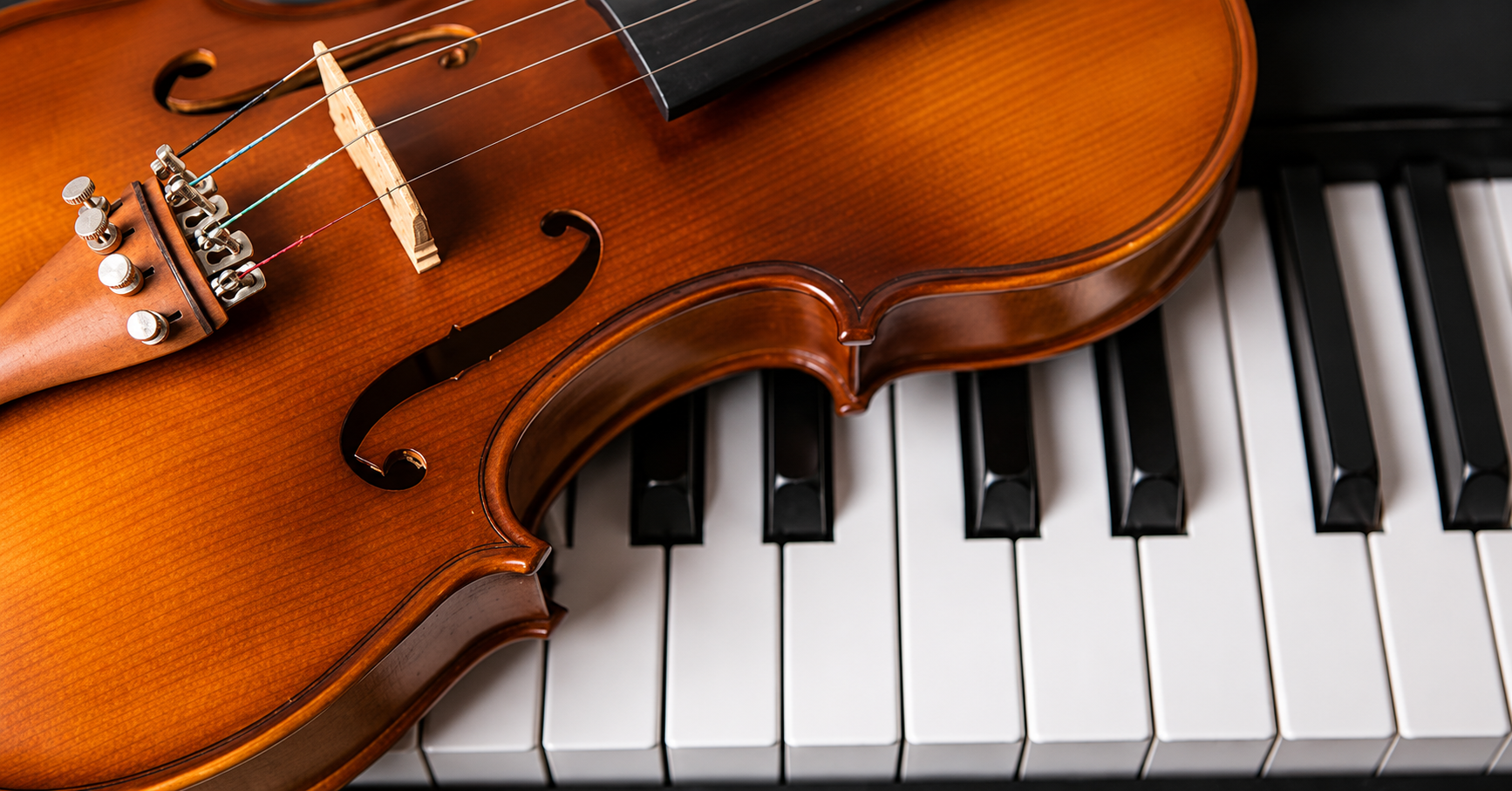 A violin resting on the keys of a piano, showing the contrast between the wooden instrument and the black and white piano keys.