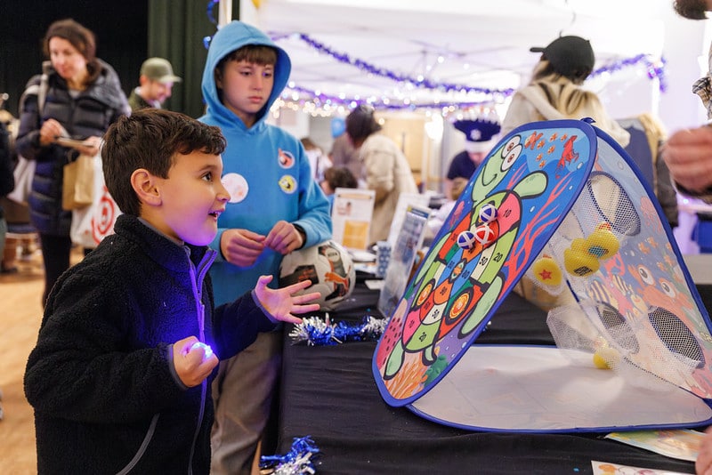 A boy throwing a beanbag at a colorful turtle-themed target game at a fair.