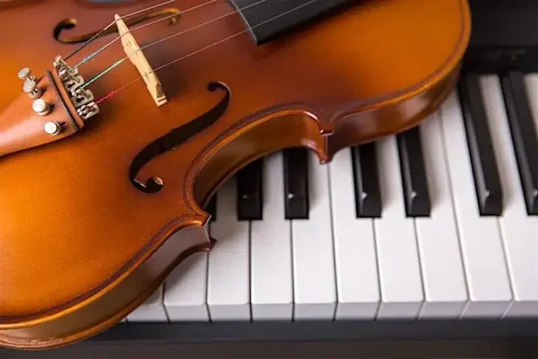 A violin rests on top of piano keys, displaying the instrument’s wood grain and strings against the black and white keys of the keyboard.